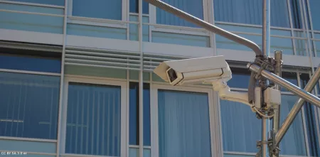 Detailaufnahme einer Videoüberwachungskamera vor einer großen Fensterfront.