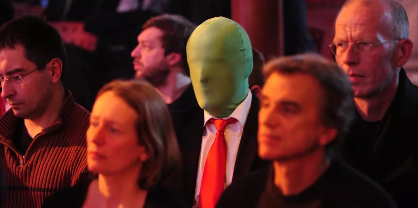 Eine Person mit einer grünen Maske im Publikum der BigBrotherAwards 2012.