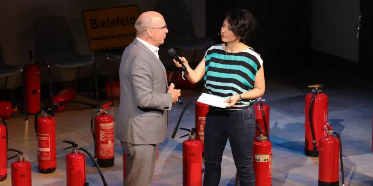 Peter Wedde wird während der BBAs 2019 auf der Bühne interviewt. Im Hintergrund eine Menge roter Feuerlöscher.