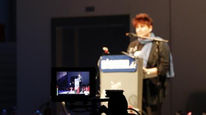 Rena Tangens am Redner.innenpult abgebildet auf einem Kameramonitor.