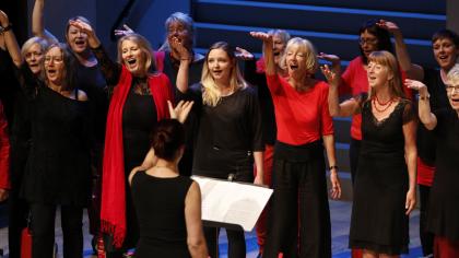 Der Chor "One Voice" sing auf der Bühne (Kleidung in schwarz/rot).