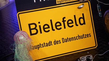 Bühnendeko: Ortseingangsschild von Bielefeld. Darunter der Text: „Hauptstadt des Datenschutzes“.