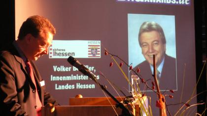 Fredrik Roggan am Redner.innenpult. Im Hintergrund ein Foto von Volker Bouffier.