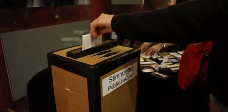 Ein Stimmzettel zum Publikumspreis wird in eine Wahlurne gesteckt.