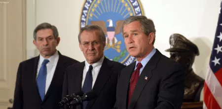 George W. Bush neben zwei weiteren Person in der Seitenansicht.