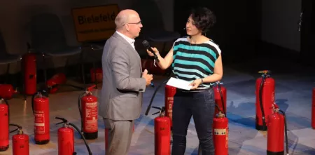 Peter Wedde wird während der BBAs 2019 auf der Bühne interviewt. Im Hintergrund eine Menge roter Feuerlöscher.