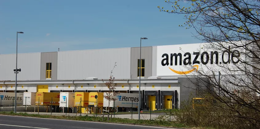 Ein Amazon-Logistikzentrum aus der Ferne. Vor dem Gebäude stehen mehrere LKWs.