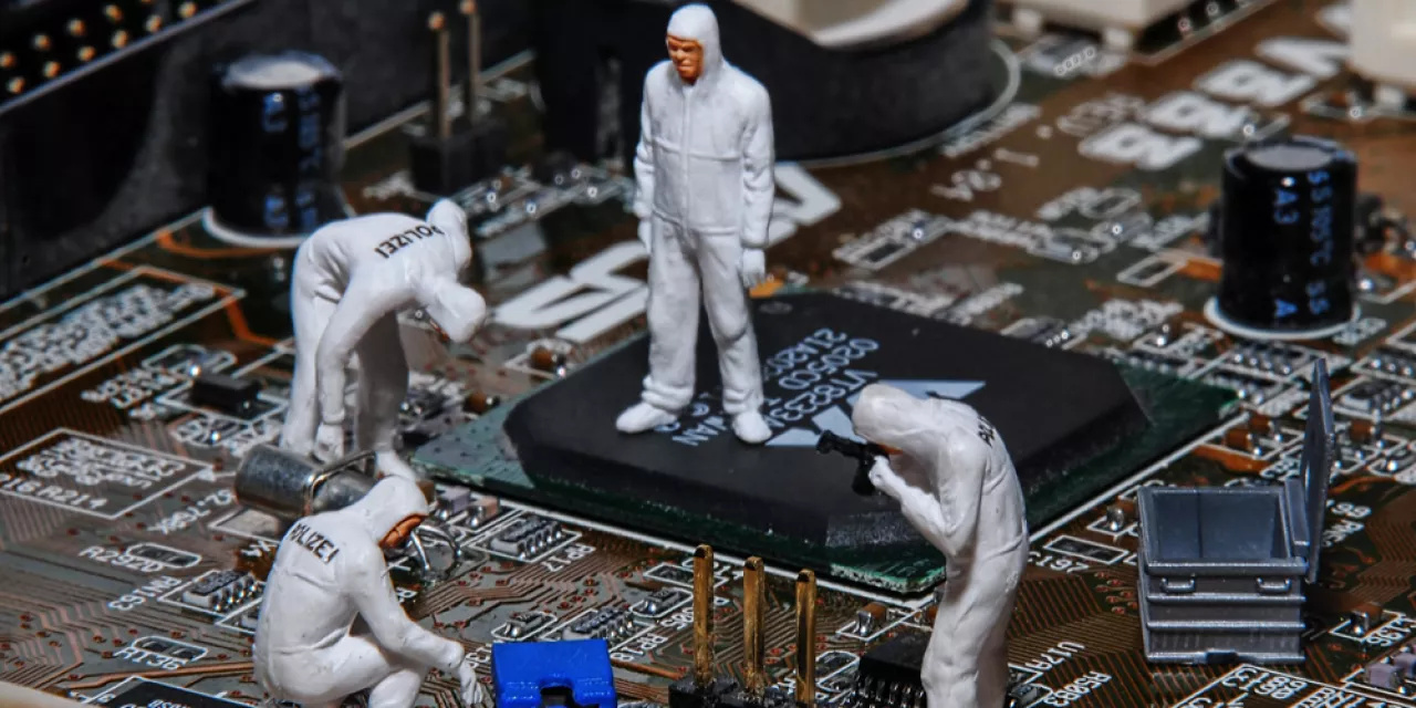 Ein Motherboard. Darauf kleine Figürchen der Spurensicherung in Schutzanzügen.