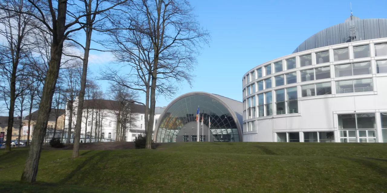 Außenansicht der Stadthalle Bielefeld, im Vordergrund eine Wiese mit Bäumen.