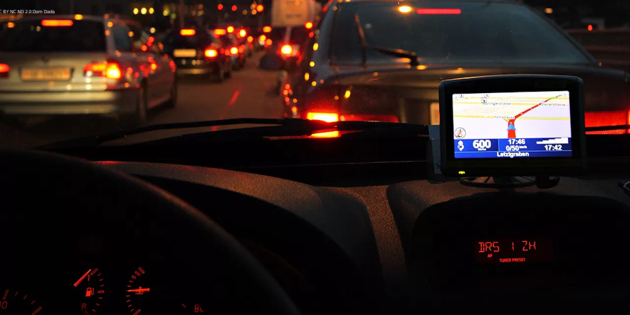 Point of view: Fahrer.innensitz eines Autos. Stau auf der Straße. Es ist dunkel. Ein Navi leuchtet.