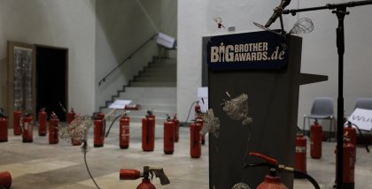 Die dekorierte Bühne der BBAs 2019 bestehend aus aufgereihten Feuerlöschern, dazwischen das Redner.innenpult.