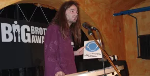 Sebastian Lisken am Redner.innenpult mit einem Schild in der Hand.