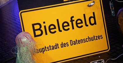 Bühnendeko: Ortseingangsschild von Bielefeld. Darunter der Text: „Hauptstadt des Datenschutzes“.