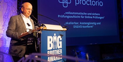 Peter Wedde am Redner.innenpult. Im Hintergrund das Proctorio-Logo.
