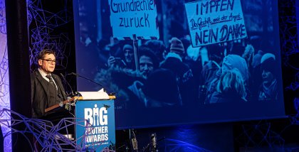 padeluun am Redner.innenpult. Im Hintergrund ein Foto einer Demo.