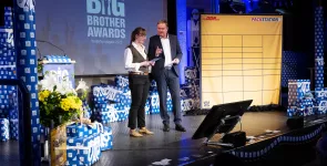 Moderatorin Julia Witte und Moderator Andreas Liebold auf der Bühne. Im Hintergrund eine DHL Packstation (Deko).