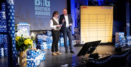 Moderatorin Julia Witte und Moderator Andreas Liebold auf der Bühne. Im Hintergrund eine DHL Packstation (Deko).