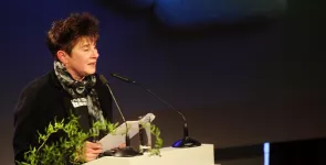 Rena Tangens am Redner.innenpult. Im Hintergrund eine Strichfigur, die auf einer Wolke liegt.