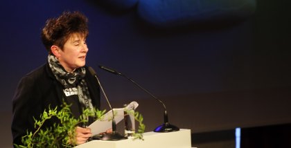 Rena Tangens am Redner.innenpult. Im Hintergrund eine Strichfigur, die auf einer Wolke liegt.