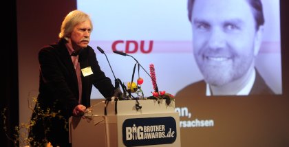 Rolf Gössner am Redner.innenpult. Im Hintergrund eine Portraitaufnahme von Uwe Schünemann und das Logo der CDU.