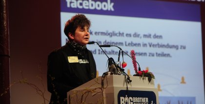 Rena Tangens am Redner.innenpult der BigBrotherAwards 2011. Im Hintergrund ein Screenshot der Startseite von Facebook.