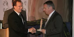 Fredrik Roggan (links) übergibt den BigBrotherAward an den Datenschutzbeauftragten (rechts) der Telekom. Er hält die Statue breits in der Hand.
