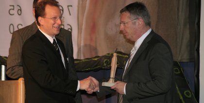 Fredrik Roggan (links) übergibt den BigBrotherAward an den Datenschutzbeauftragten (rechts) der Telekom. Er hält die Statue breits in der Hand.