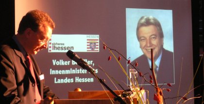 Fredrik Roggan am Redner.innenpult. Im Hintergrund ein Foto von Volker Bouffier.