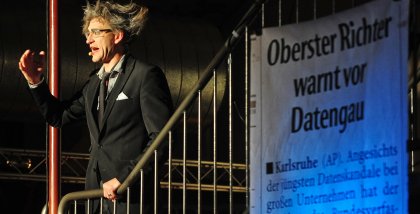 Eine Person mit zauseligen Haaren auf einer Treppe. Rechts daneben ein Banner mit der Aufschrift „Oberster Richter warnt vor Datengau“.