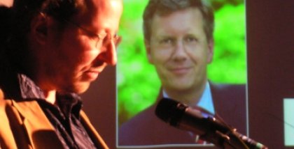 Werner Hülsmann am Redner.innenpult. Im Hintergrund ein Foto von Christian Wulff.