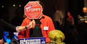 Alvar Freude am Redner.innenpult. Vor sein Gesicht wird ein Stopp-Zeichen gehalten.