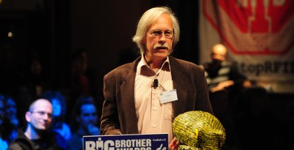 Rolf Gössner am Redner.innenpult. Darauf die Datenkrake.