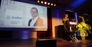 padeluun am Redner.innenpult. Im Hintergrund das Prudsys-Logo sowie ein Portraitfoto von Jens Scholz (Vorstand).