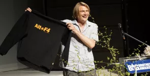 Frank Rosengart hält einen schwarzen Pullover hoch. Darauf steht: „Alt+F4“.