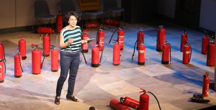 Moderatorin Golineh Atai auf der Bühne. Im Hintergrund viele Feuerlöscher.