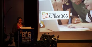 Leena Simon am Redner.innenpult. Im Hintergrund ein Werbefoto von Office 365.